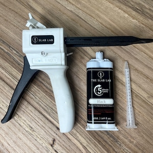 May include: A white and black epoxy dispenser, a black epoxy cartridge, and a clear mixing nozzle. The cartridge is labelled "THE SLAB LAB 5 Minute Epoxy Black" and contains 50ml (1.69 fl oz).