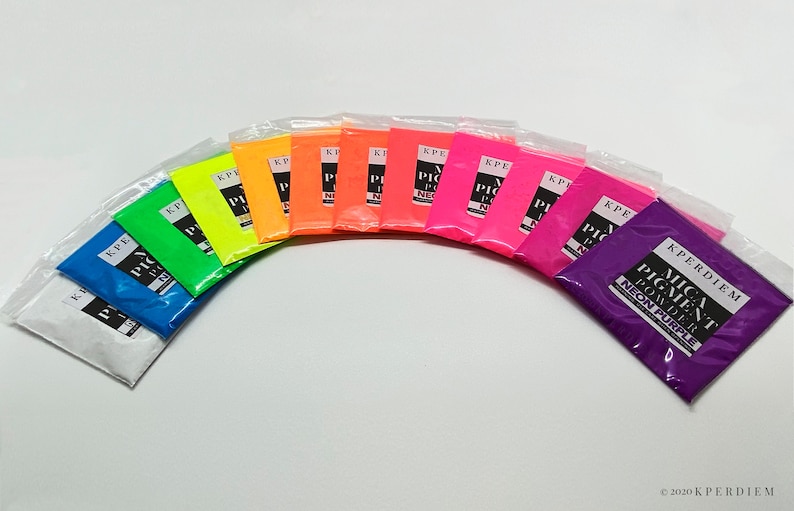 May include: A set of 12 small bags of neon mica pigment powder. The bags are arranged in a semi-circle, with the colors ranging from white to purple. Each bag has a black label with the text "KPERDIEM MICA PIGMENT POWDER NEON [COLOR]" printed on it.