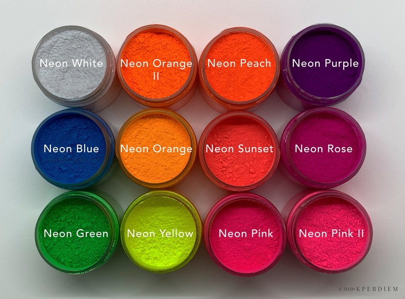 Op de afbeelding: Twaalf ronde potjes met levendige pigmentpoeders in diverse neonkleuren, waaronder wit, oranje, perzik, paars, blauw, sunset, rose, groen, geel en roze. Elk potje is voorzien van een label met de bijbehorende kleurnaam in witte tekst.