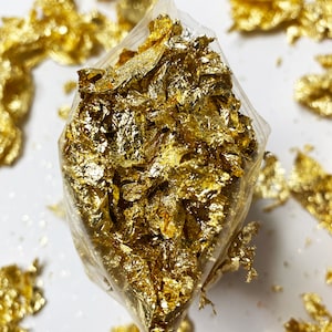 May include: A clear plastic bag filled with gold leaf flakes. The flakes are scattered around the bag on a white surface. The text "© 2020 KPERDIEM DESIGN CO." is in the upper right corner.