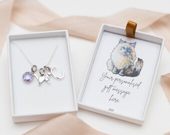 May include: A silver necklace with a round lavender crystal charm, an origami cat charm, and a letter C charm. The necklace is inside a white gift box next to a card featuring a cat illustration and the text Your personalised gift message here.
