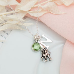 Puede incluir: Un collar de plata con una piedra preciosa verde, un dije de letra de plata y un dije de gnomo de plata.