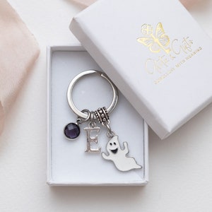 May include: A silver keyring with a purple gemstone, a letter E charm, and a ghost charm. The keyring is in a white box with the text "Gifts" and "Engraved with Meaning".