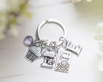May include: Silver keychain with a cupcake, a mixer, a cookbook charm, and the letter E. The charms are attached to a silver key ring.