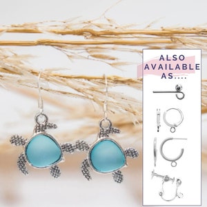 Puede incluir: Pendientes de plata con forma de tortuga con detalles de cristal azul claro. Los pendientes se muestran sobre un fondo de hierba seca. El texto "TAMBIÉN DISPONIBLE COMO..." se muestra en un cuadro rosa con contorno blanco. La caja contiene imágenes de diferentes estilos de pendientes.