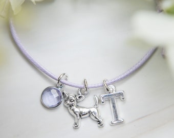 May include: A lavender cord bracelet with three charms: a silver chihuahua, a silver letter "T", and a clear purple gemstone.
