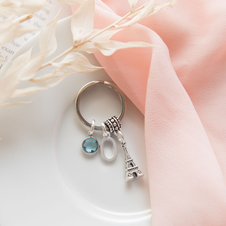 May include: A silver keychain with a blue crystal charm, a silver letter O charm, and a silver Eiffel Tower charm.