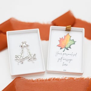 May include: Two silver maple leaf earrings in a white box with a white box with a watercolour illustration of a maple leaf and the text "Your personalised gift message here xxx"