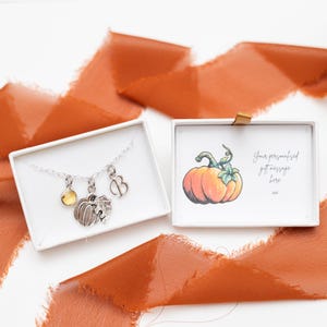 May include: A silver necklace with a pumpkin charm, a small leaf charm, a yellow gemstone, and a letter "B" charm. The necklace is in a white box with a card that says "Your personalised gift message here".