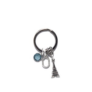May include: Silver keychain with a blue gemstone, a silver letter O charm, and a silver Eiffel Tower charm.