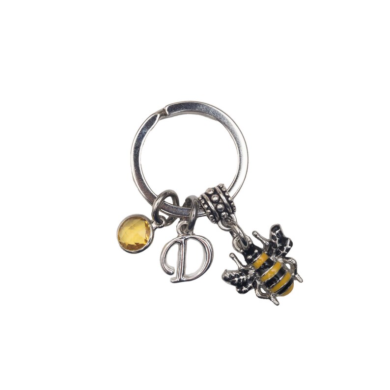 May include: Silver-tone keychain with a bee charm, a yellow gemstone, and a letter "D" charm. The bee charm is black and yellow. The keychain is on a white background.