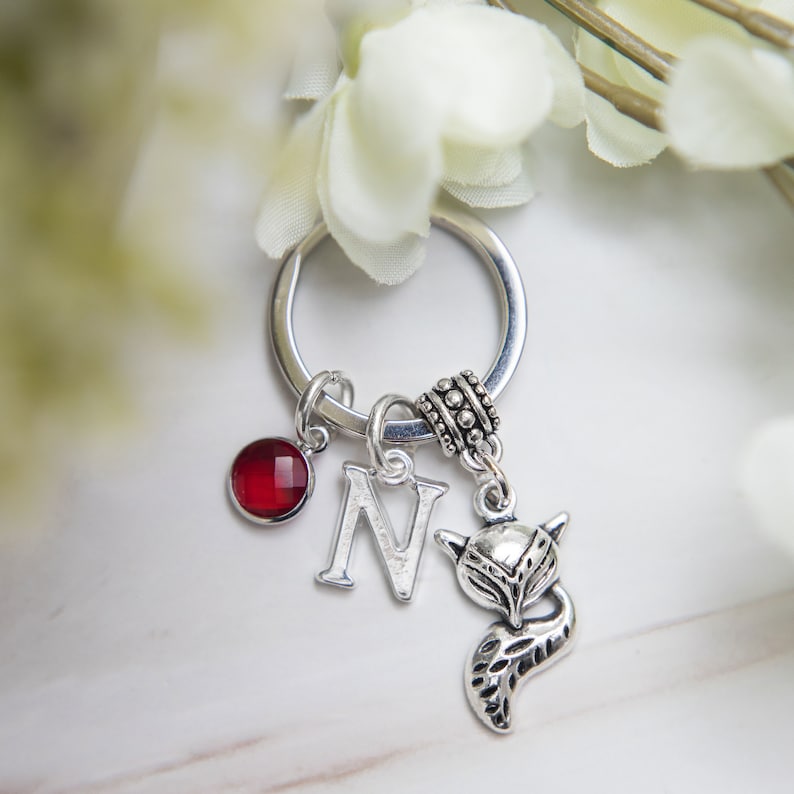 Puede incluir: Llavero de plata con una piedra preciosa roja, un dije de letra N de plata y un dije de zorro de plata.