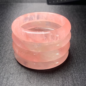 Op de afbeelding: Vier gestapelde roze kwarts armbanden, elk met een gladde, gepolijste afwerking. De armbanden zijn lichtroze met subtiele witte strepen.