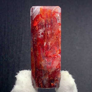 May include: A rectangular, polished crystal with a vibrant red and orange color palette. The crystal's surface displays a complex, layered internal structure, with variations in transparency and texture. The top is a flat, rectangular shape.
