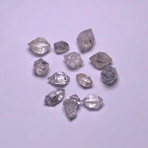 Puede incluir: Una colección de doce cristales de diamante natural, transparentes y facetados. Los cristales son de varios tamaños y formas, algunos tienen un ligero tono gris.