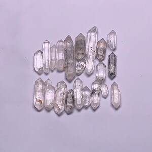 Puede incluir: Una colección de puntas de cristal de cuarzo transparente, también conocidas como cristales de cuarzo doblemente terminados. Los cristales son de varios tamaños y formas, algunos tienen una apariencia ahumada o nublada.