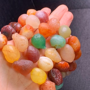 May include: A collection of colourful agate beads in various shapes and sizes. The beads are a mix of red, orange, yellow, green, and brown.