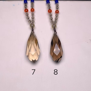 May include: Two necklaces with teardrop-shaped pendants. The pendants are a light brown color and are faceted. The necklaces have a beaded chain with orange, clear, and blue beads. The numbers 7 and 8 are below the pendants.