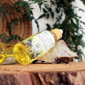 Puede incluir: Dos botellas de vidrio &aacute;mbar con goteros y tapas de madera, llenas de un l&iacute;quido amarillo. Las botellas est&aacute;n etiquetadas con "Garden Goodness" y tienen un dise&ntilde;o floral. Las botellas est&aacute;n sobre una superficie de madera con una roca y follaje verde en el fondo.