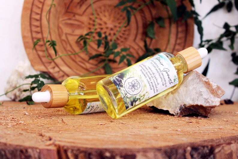 Puede incluir: Dos botellas de vidrio &aacute;mbar con goteros de bamb&uacute; llenas de un l&iacute;quido amarillo. Las botellas est&aacute;n etiquetadas con "Hair Growth" y contienen una mezcla de aceites para estimular el crecimiento del cabello y curar el cuero cabelludo. Las botellas est&aacute;n sobre una superficie de madera con una roca blanca.