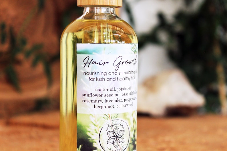 Puede incluir: Una botella de vidrio transparente con una tapa de madera, etiquetada como "Hair Growth" y que enumera ingredientes como aceite de ricino, aceite de jojoba, aceite de semilla de girasol, romero, lavanda, menta piperita, bergamota y madera de cedro.