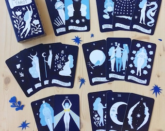 May include: A tarot card deck featuring navy blue cards with white and light blue illustrations. The deck includes cards with images of figures, celestial bodies, and symbols. The box reads "The Cosmic Woman Tarot".