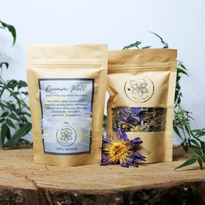 May include: Two brown paper bags with a clear window, containing dried herbs and flowers. The bags are labeled "Dream Well" and list the ingredients, including blue lotus, valerian root, mugwort, and chamomile. The text "100% natural" is printed on the bag.