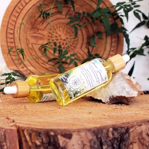 Puede incluir: Dos botellas de vidrio &aacute;mbar con goteros y tapas de madera, etiquetadas con "Flower Essence" sobre una superficie de madera. Las botellas est&aacute;n rodeadas de follaje verde y una roca blanca.