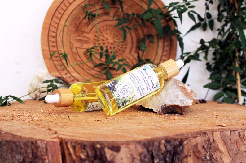 Puede incluir: Dos botellas de vidrio &aacute;mbar con goteros y tapas de madera, etiquetadas con "Flower Essence" sobre una superficie de madera. Las botellas est&aacute;n rodeadas de follaje verde y una roca blanca.