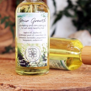 Puede incluir: Una botella de vidrio transparente con un gotero de bamb&uacute; lleno de un l&iacute;quido amarillo. La etiqueta dice "Hair Growth nourishing and stimulating oil for lush and healthy hair" y enumera los ingredientes, que incluyen aceite de ricino, aceite de jojoba, aceite de semilla de girasol, aceites esenciales, romero, lavanda, menta piperita, bergamota y madera de cedro. La etiqueta tambi&eacute;n dice "100% natural".