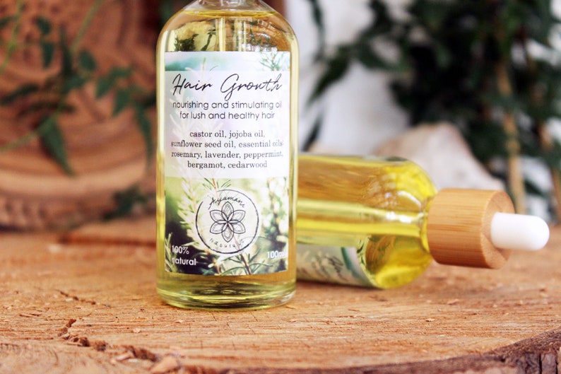 Puede incluir: Una botella de vidrio transparente con un gotero de bamb&uacute; lleno de un l&iacute;quido amarillo. La etiqueta dice "Hair Growth nourishing and stimulating oil for lush and healthy hair" y enumera los ingredientes, que incluyen aceite de ricino, aceite de jojoba, aceite de semilla de girasol, aceites esenciales, romero, lavanda, menta piperita, bergamota y madera de cedro. La etiqueta tambi&eacute;n dice "100% natural".