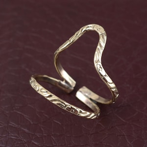 May include: A gold-toned metal ring with a wavy, textured design. The ring is open and adjustable.