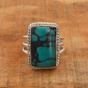 Könnte beinhalten: Ein silberner Ring mit einem rechteckigen Türkis-Stein, der in einer seilartigen Umrandung gefasst ist. Der Stein hat eine dunkelblaue und grüne Farbe mit schwarzen Adern.