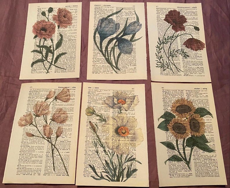 May include: Six vintage dictionary pages featuring floral illustrations. Each page showcases a different flower, including a poppy, a bluebell, a sunflower, and a white flower. The pages are printed on aged paper with a yellowed hue.