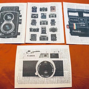 May include: Three black and white prints of vintage cameras on a brown surface. The first print features a Rolleiflex camera. The second print features a grid of 16 different camera images. The third print features a Polaroid Pronto 600 camera. The fourth print features a Canon camera.
