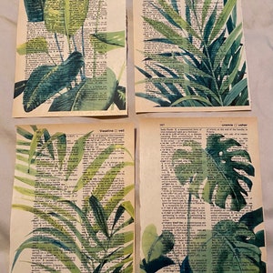 May include: Four pages from a vintage dictionary with watercolor illustrations of tropical plants. The pages are in shades of green and brown with the text "vagrom", "value-added tax", "vapid", "vasectomy", "Vaseline", "veil", "uremia", and "usher" visible.
