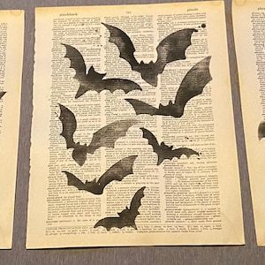 May include: Three black and white prints of bats on a vintage book page background. The bats are in various sizes and positions, creating a whimsical and spooky Halloween-themed design.