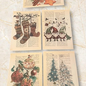 Puede incluir: Cuatro páginas de diccionario vintage con ilustraciones navideñas. La primera página muestra una rama de pino con una estrella, una naranja y palitos de canela. La segunda página muestra tres calcetines colgando de una rama. La tercera página muestra tres gnomos sosteniendo adornos navideños. La cuarta página muestra un árbol de Navidad y adornos.