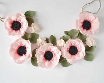 May include: A pink felt flower garland with green leaves and white felt flowers. The garland is strung on twine and is perfect for decorating a nursery or children's room.