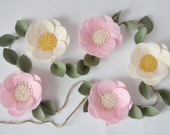 May include: A garland of felt flowers with pink and white flowers and green leaves. The garland is strung with twine.