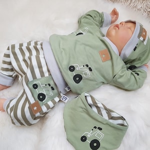 Könnte beinhalten: Ein Baby-Outfit-Set in Olivgrün und Weiß. Das Set beinhaltet ein Kapuzenoberteil, eine gestreifte Hose und ein Lätzchen. Das Oberteil und das Lätzchen zeigen eine Traktorgrafik. Die Hose hat olivgrüne und weiße Streifen. Das Outfit ist für ein Neugeborenes konzipiert.