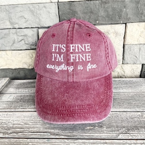 May include: A burgundy red baseball cap with white embroidered text that reads "It's fine I'm fine everything is fine."