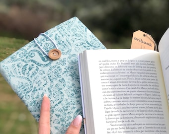 May include: A teal blue notebook with a white string closure and a wooden button. The notebook is open to a page with text in Spanish. The text reads "aribook" in the upper right corner.