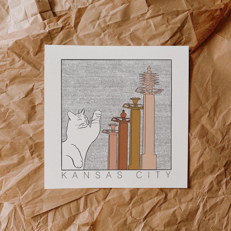 May include: A black and white illustration of a cat looking up at a row of five buildings with the text "KANSAS CITY" below. The buildings are stylized and have a retro look.