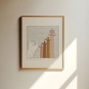 May include: A framed illustration of a white cat looking up at a row of buildings with the text "KANSAS CITY" below.