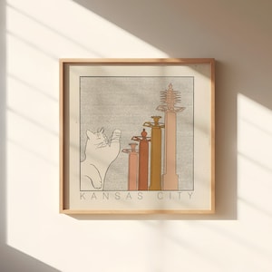 May include: A framed print with a white cat illustration and a line drawing of five buildings with the text "KANSAS CITY" at the bottom.