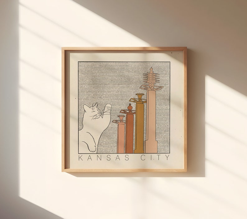 May include: A framed print with a white cat illustration and a line drawing of five buildings with the text "KANSAS CITY" at the bottom.