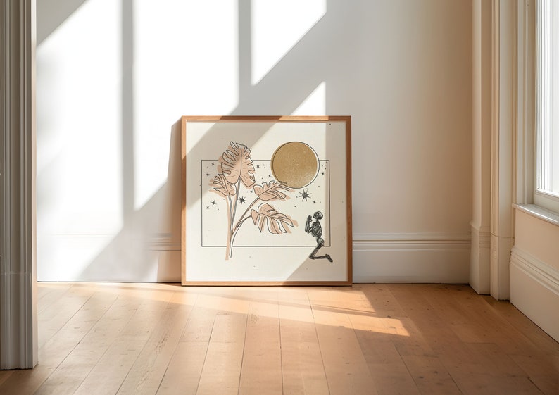 Op de afbeelding: Een ingelijst print met een minimalistische illustratie van een skelet dat knielt voor een grote, gouden maan. Het skelet wordt omringd door gestileerde bladeren en sterren.