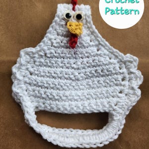 May include: A white crochet chicken-shaped kitchen towel holder with a red comb and yellow beak. The holder has googly eyes and a loop for hanging. The text "Crochet Pattern" is in a white circle.