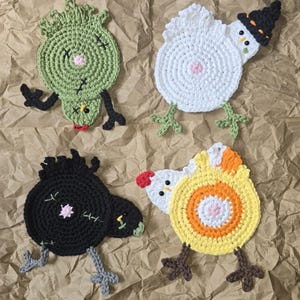 May include: Four round crochet coasters shaped like chickens. One is green with black stitches, one is white with a black witch hat, one is black with green stitches, and one is yellow, orange, and white with a red comb and orange beak.